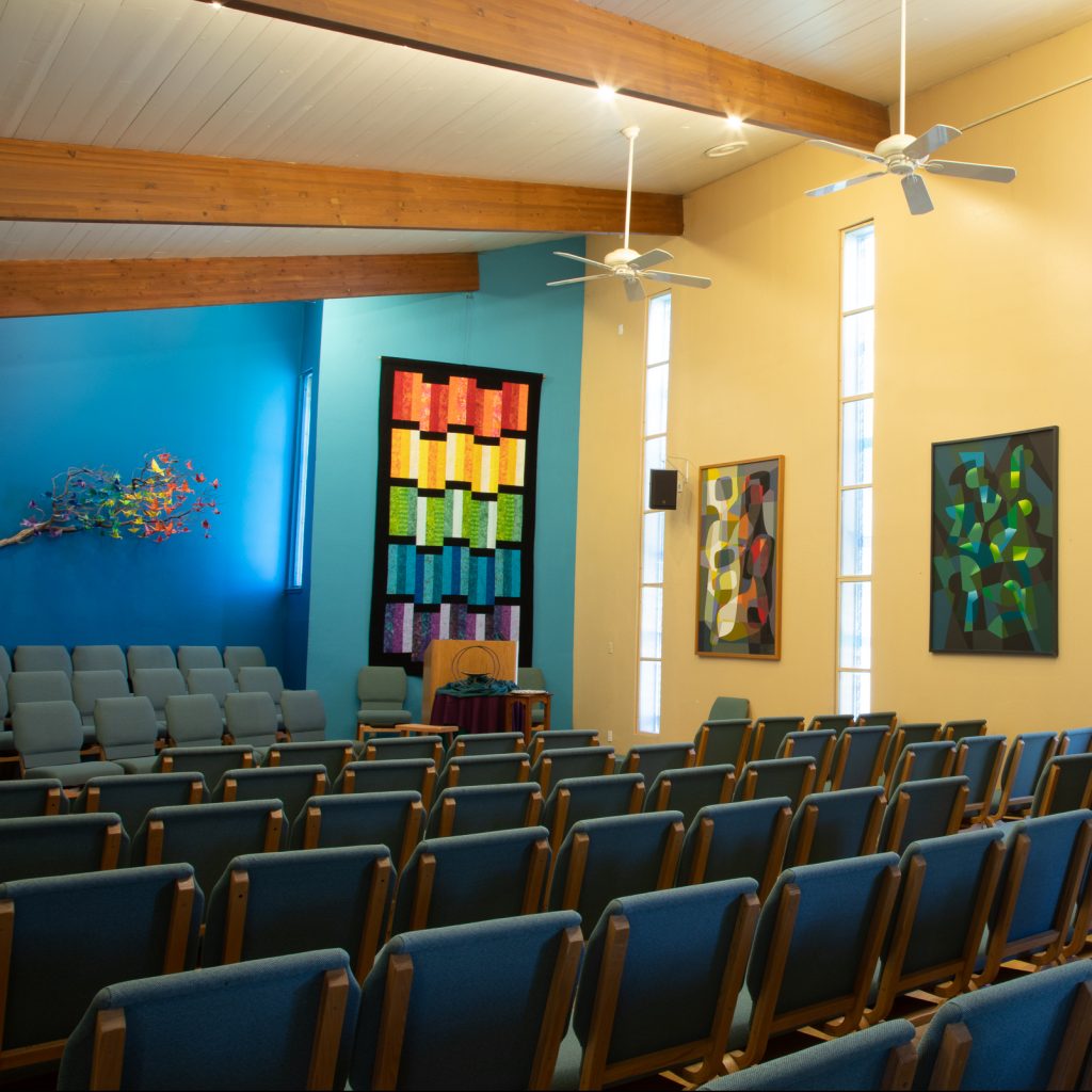 Our sanctuary has a high-ceiling and exposed beams. It has blue accent walls at one end with a rainbow quilt and collection of folded cranes hanging.