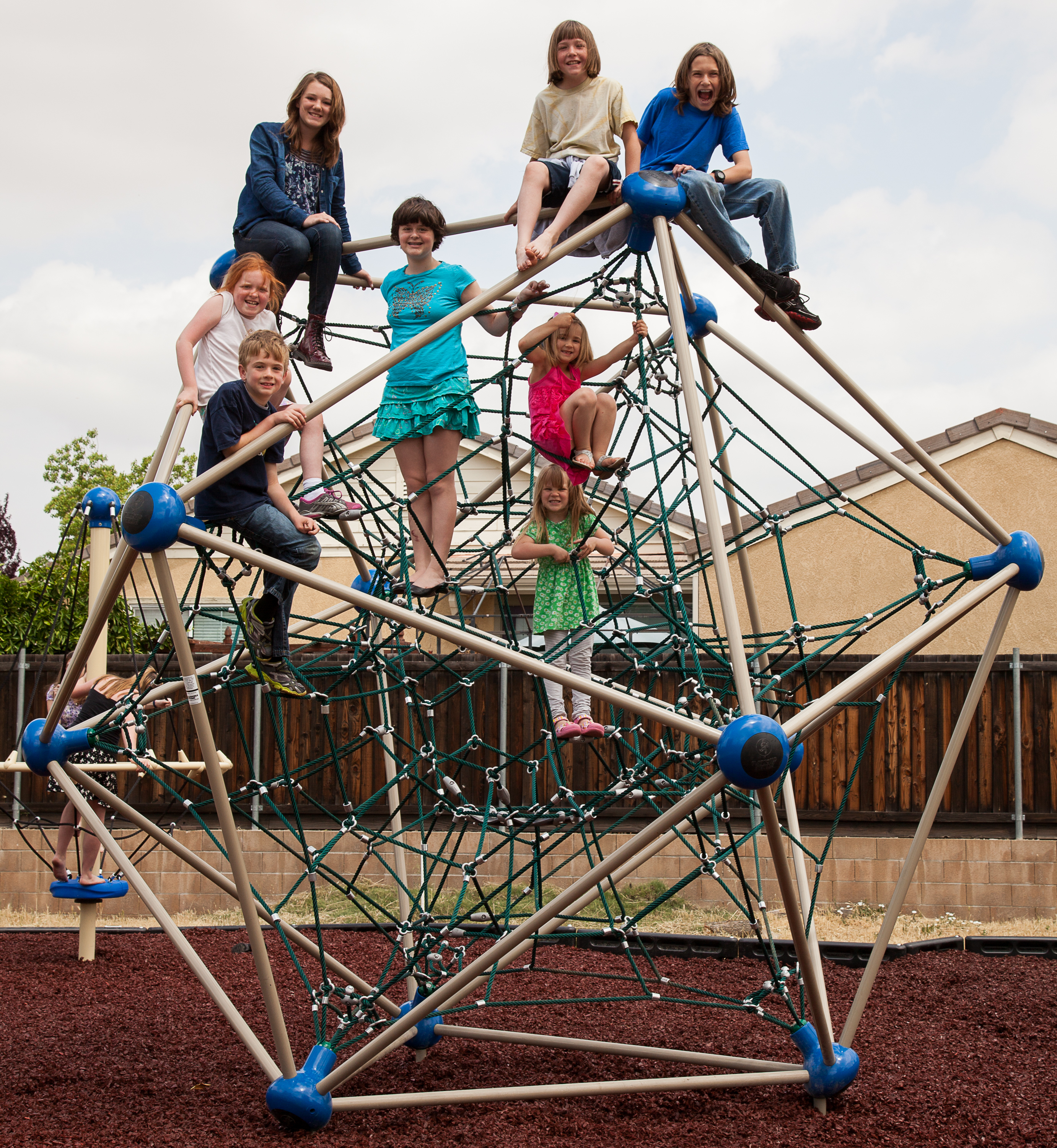 A group of children sit on a climbing structure on a playground.