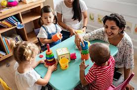Two women play with three young kids at a table