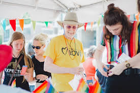 Members smiling and talking while standing at a booth during a Pride event