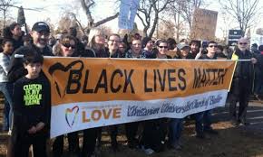 Large group of people stand behind a banner that reads "Black Lives Matter"