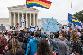 A group of people hold signs about equal rights and flags, while standing in front of the United States Supreme Court Building